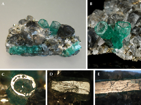 Figure 17. A: In sample 17 (26 mm long), a base of black shale (not visible) is covered with albite, calcite, and pyrite crystals. In this matrix, five emerald crystals are embedded, two of them as deep cups (center) and three as “normal” emeralds (lower right and left). B: Details of the two emerald cups (5.5 mm long on the right). C: In reflected light, the basal plane of one cup appears bright together with the basal faces of small hillocks or columns in the cup. D: Growth steps on the surface of one <em>m</em> prism face of a cup. E: Growth steps on the surface of the <em>m</em> prism face of a “normal” emerald crystal. Photos by K. Schmetzer (A, C–E) and G. Martayan (B); field of view 7.6 mm (C–E).