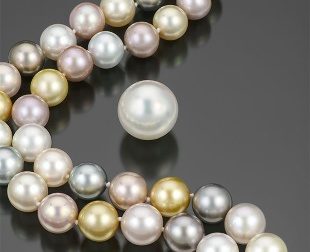 Figure 11. A mixed strand of 79 pearls ranging from 11.8 to 14.8 mm, consisting of pink Chinese freshwater, black Tahitian, golden Indonesian, and white Australian bead cultured pearls. Also pictured is an exceptionally large 20.4 mm South Sea bead cultured pearl weighing 12 g. Photo by Robert Weldon; courtesy of Yoko London.