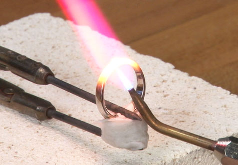 先端がタングステンカーバイドまたはプラチナのピンセットでプラチナリングを固定する。 傷を防ぐために数枚のティッシュを重ねて、リングとピンセットの間にあてる。 Firecoat溶液で中央の石をカバーする。 高熱から保護するために、ウェットティッシュで包む。 1700プラチナシームレス修理はんだを使用する。 トーチの接続部を持って、リングの内側を予熱。 炎の内側のコーン型のすぐ上の部分がこの位置にくるようにトーチを配置し、その後、継ぎ目の真上にトーチを持ってきて、継ぎ目とはんだを直接熱する。はんだが溶けて継ぎ目に流れ出たら、すぐにトーチを離す。 ウェットティッシュや先がカーバイド素材のピンセットがヒートシンクの役割となり継ぎ目から熱を奪うので、炎は強火でなければならない。