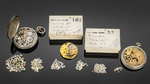 Figure 6. Watch bearings fashioned out of Montana sapphires in various stages of completion. The leftmost pile contains rough sapphires ready for fabrication, and the pile second from the left contains sapphires ground to wafers of standard thickness to be drilled out to produce bearings. The four piles to the right show finished natural sapphire watch bearings. Photo by Robert Weldon; courtesy of the Sapphire Gallery.