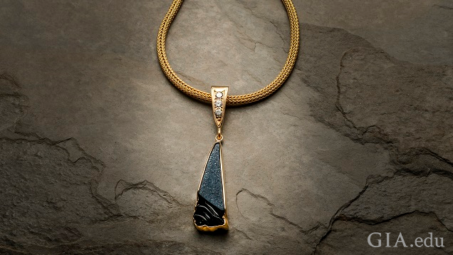 縁が14Kイエローゴールドで囲まれている三角形のブラックオニキス晶洞の彫刻。3つの0.10ctのダイヤモンドがセットされた三角形の形をしたゴールドのバチカンでゴールドチェーンにつり下げられている。