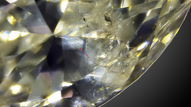 Figure 2. A marquise-shaped diamond set in one of the earrings displays a cloudy appearance (indicated by arrow) caused by the presence of filler material within surface-reaching fractures. Photo by Gaurav Bera.