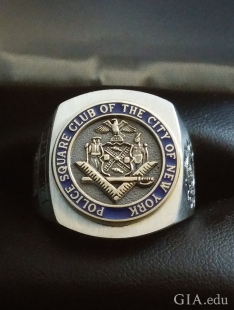 一枚中心为圆圈且带有浮雕标志的方形戒指。上面刻有“Police Square Club of the City of New York”（纽约市警察局共济会）。