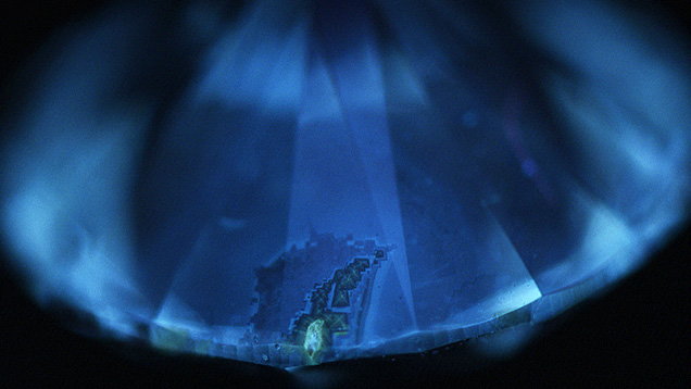 Figure 3. When exposed to deep-UV excitation, the bulk of the diamond showed blue surface fluorescence, whereas the yellow color zones and the cross patterns with visibly darker particles showed weak yellow surface fluorescence. Image by Sally Eaton-Magaña.