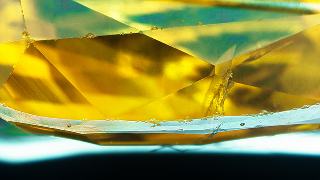 Figure 2. The appearance of laser ablation spots on a faceted yellow sapphire. There are two ablation pits on the girdle, located left and right of center. They are 55 μm in diameter and essentially undetectable without a microscope or loupe. Photomicrograph by Aaron Palke; field of view 5.21 mm.