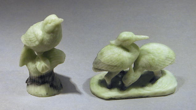 Two carved jade bird figurines: one perched on a base, the other depicting two birds standing together.