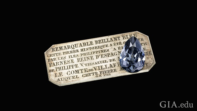 A large pear shaped diamond sits on a silver plaque with French words.