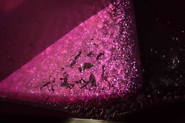 Reflective silk inclusions in the natural sapphire seed are visible behind a coarse flux fingerprint in the synthetic ruby overgrowth.