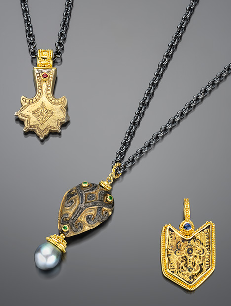 Three ornate necklaces featuring intricate pendants: one with a gold design, another with a patterned stone, and a third with a blue gem.