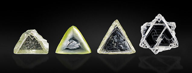 Four triangular crystals of varying colors and textures, displayed against a black background.