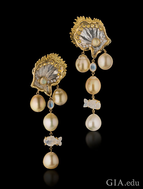 珠母贝制成的蛤蜊状镶座上，垂悬着南洋珍珠吊坠，饰以白色和黄色的蓝宝石以及 18K 黄金。从耳环上部垂悬而下的，还有月光石，包含一个鱼形饰物。
