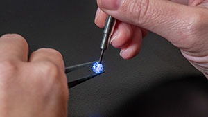 Close up of hands holding a loose stone with tweezers in one hand, and using the iD100 probe to highlight the stone in the other on a black background. Close up of hands holding a loose stone with tweezers in one hand, and using the iD100 probe to highlight the stone in the other on a black background.